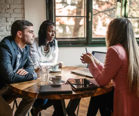 Three people having a conversation around a round table, with coffee cups and water in front of them